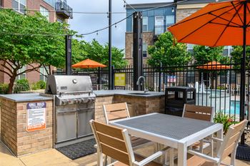 A bbq grill is on a patio with a table and chairs.